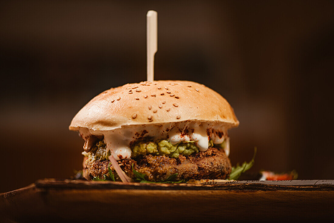 Low angle of yummy burger with vegetarian patty and grilled shiitakes between buns near sweet potato and carrot slices with alioli sauce on dark background