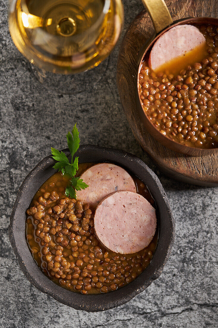 Draufsicht auf rustikale Schalen mit schmackhafter Linsensuppe mit Petersilie und Wurstscheiben auf einem Marmortisch mit Wein beim Mittagessen