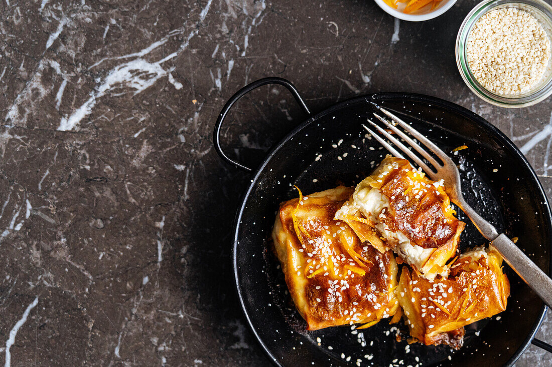 Top view of sweet tasty pastry with sesame seeds served on black plate with fork in light kitchen