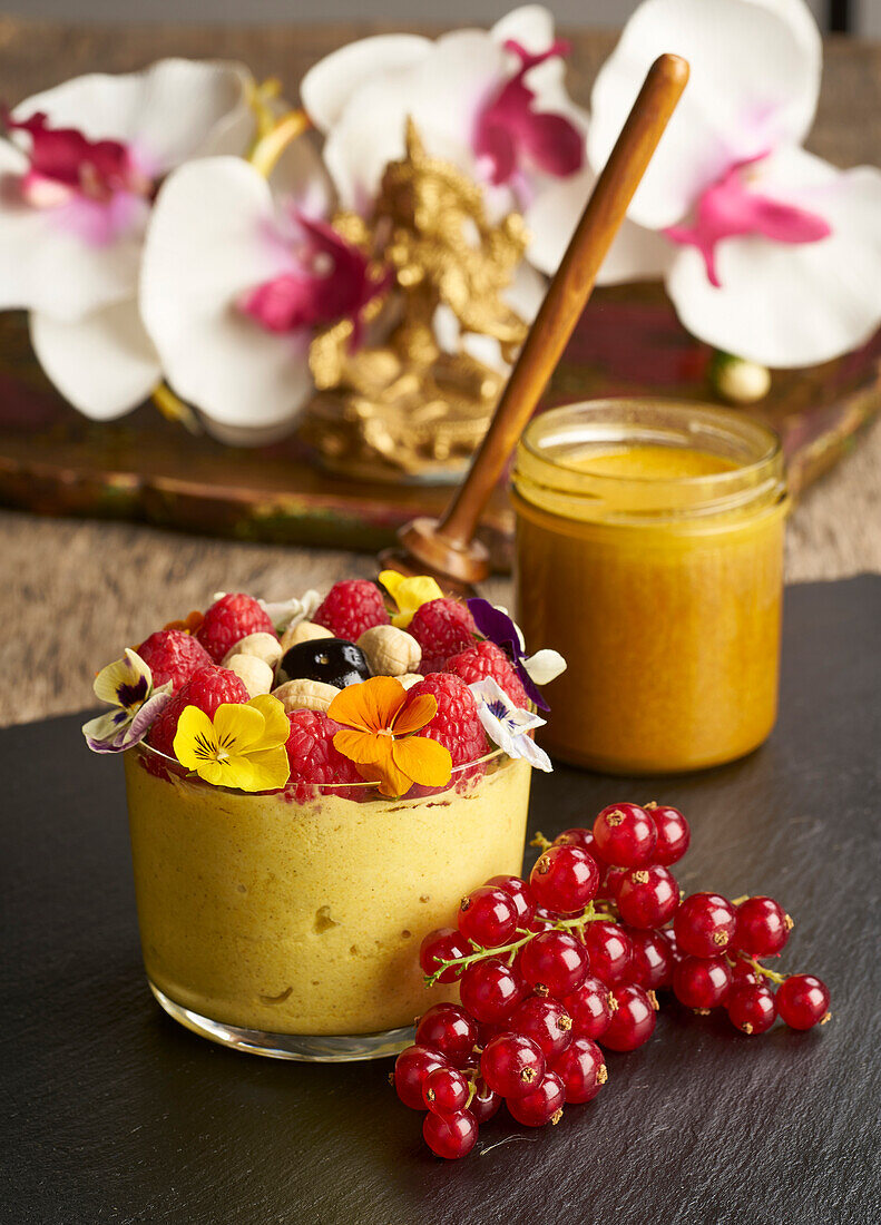 From above of glass jar with mousse dessert decorated with nuts and flowers and raspberry place on table near red currant and orchids