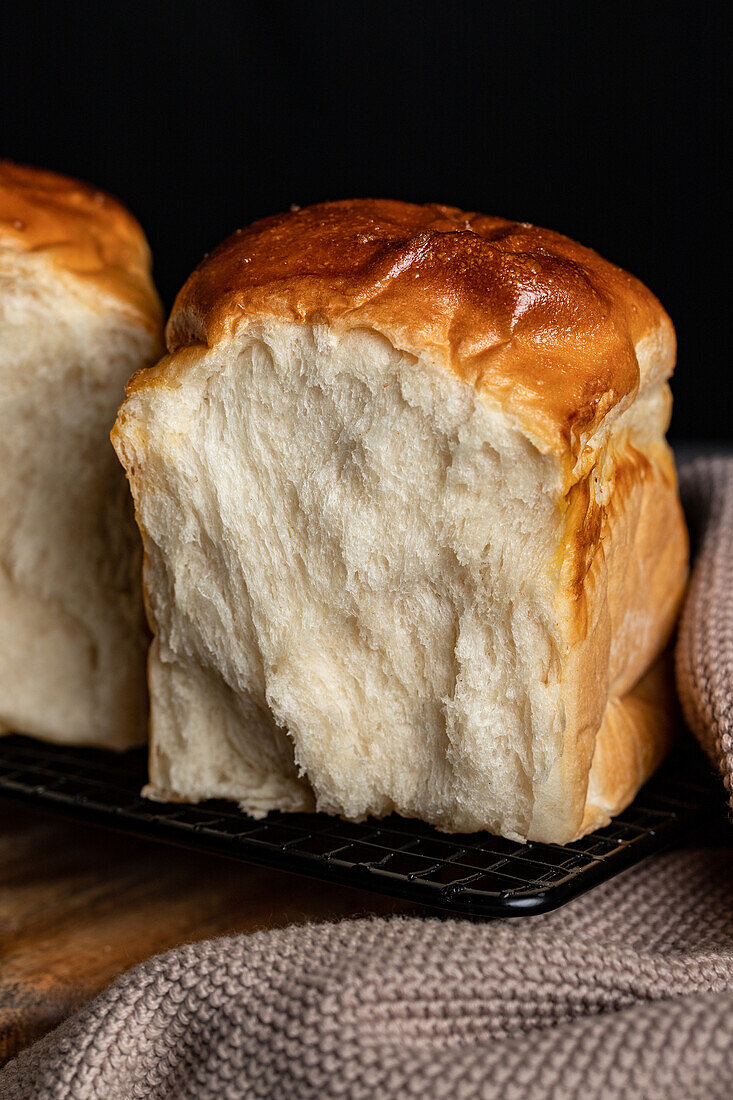 Delicious split halves of sandwich bread on grill tray placed on counter and cutting board against dark background