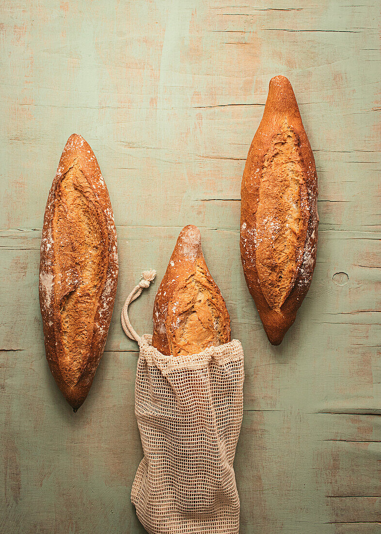 Top view composition of delicious crispy artisan sourdough bread loaves packed in burlap bags on green background