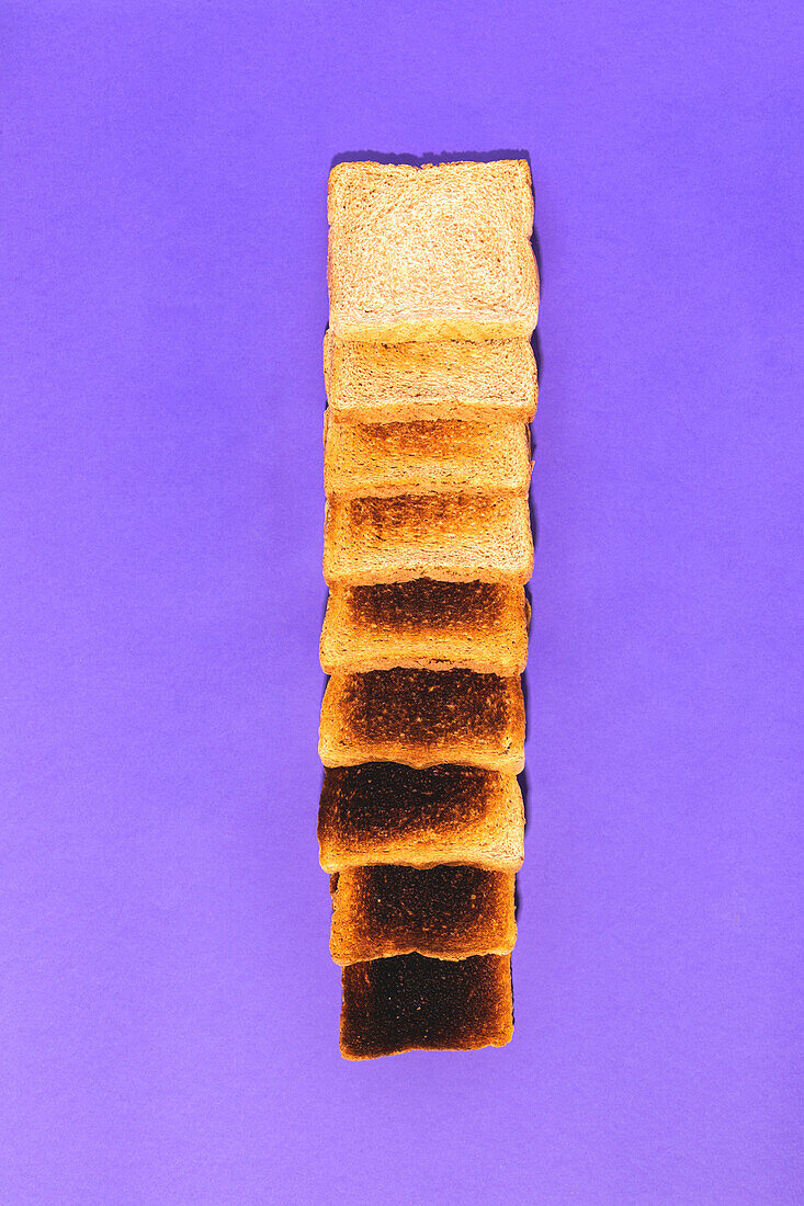 Top view of row of sliced bread ranging from fresh and soft to burnt and cracked against violet background