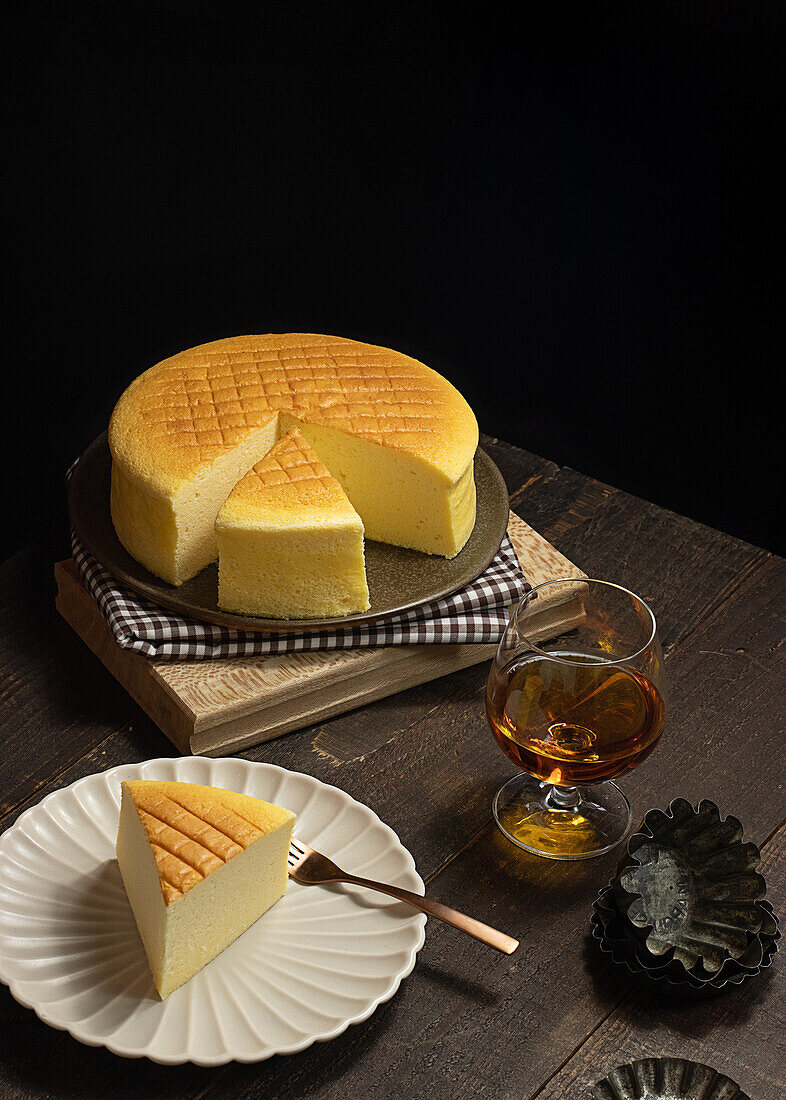 From above plates with tasty cotton cheesecake placed near glass of beverage on wooden table in dark room