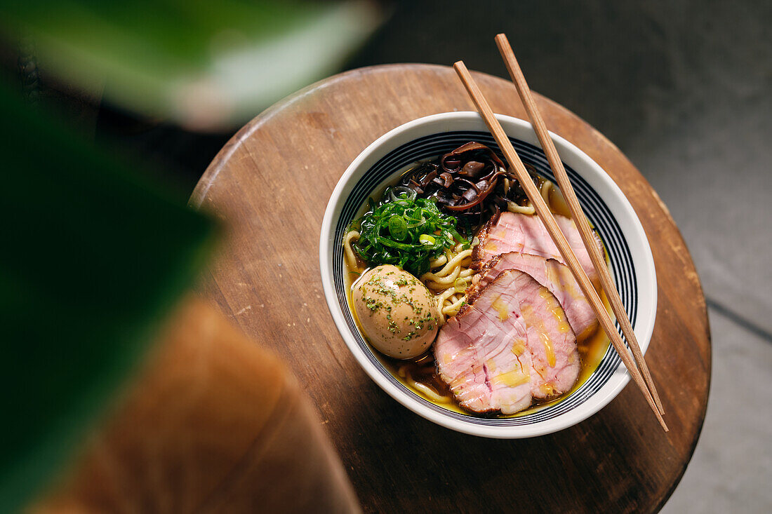 Top view of delicious traditional ramen soup in bowl with chopsticks served on round table