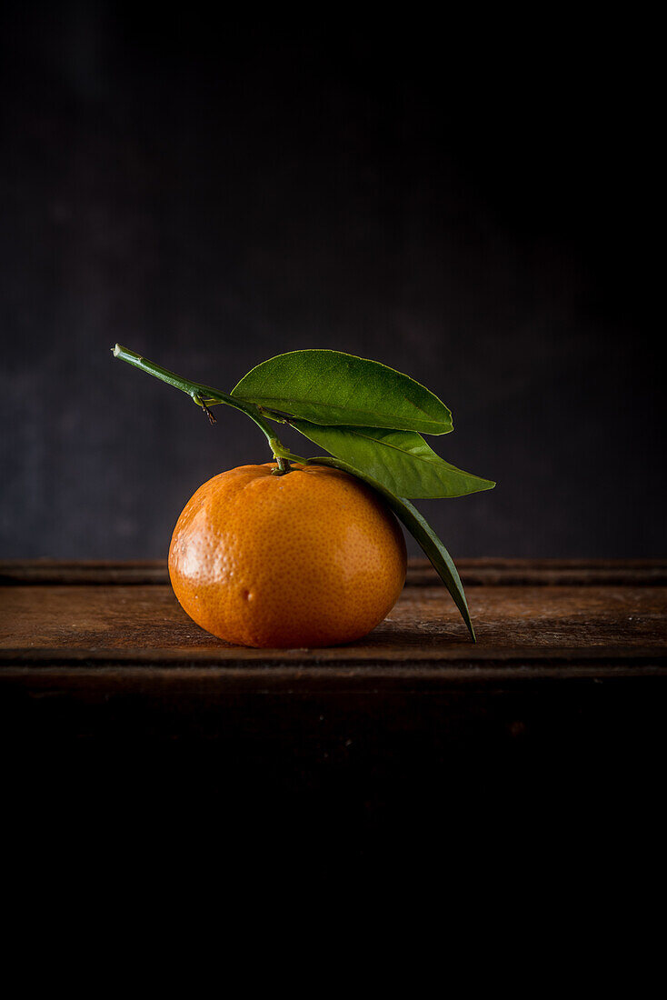 Whole unpeeled mandarin with pedicel and wavy foliage with pointed edges on wooden surface