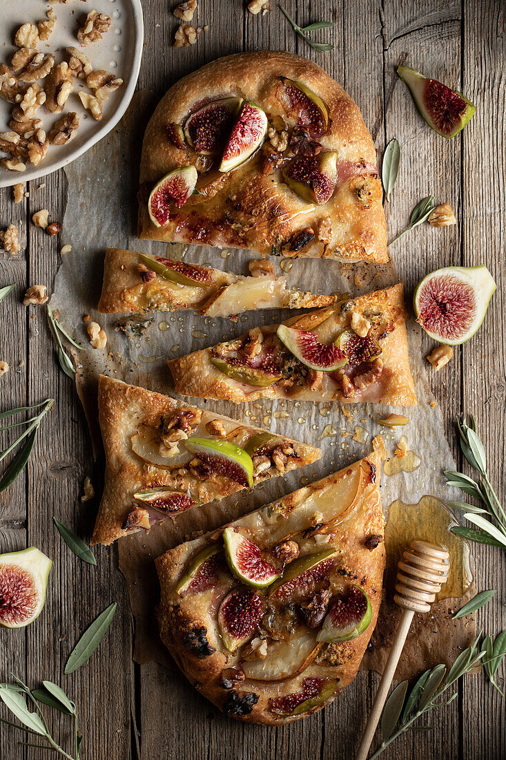 Top view of tasty baked cut flatbread with figs served on wooden table with herbs and walnuts in light kitchen