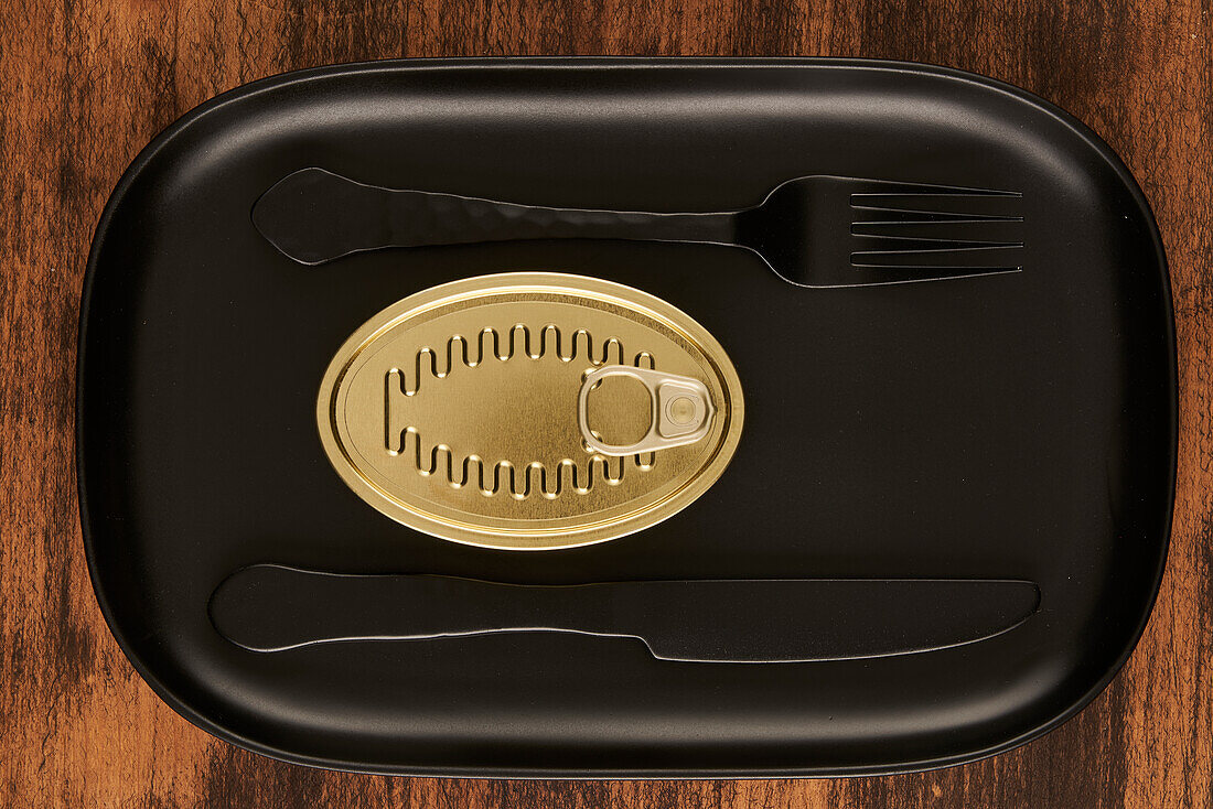 Top view of black fork and knife placed near sealed canned food on rectangular black tray