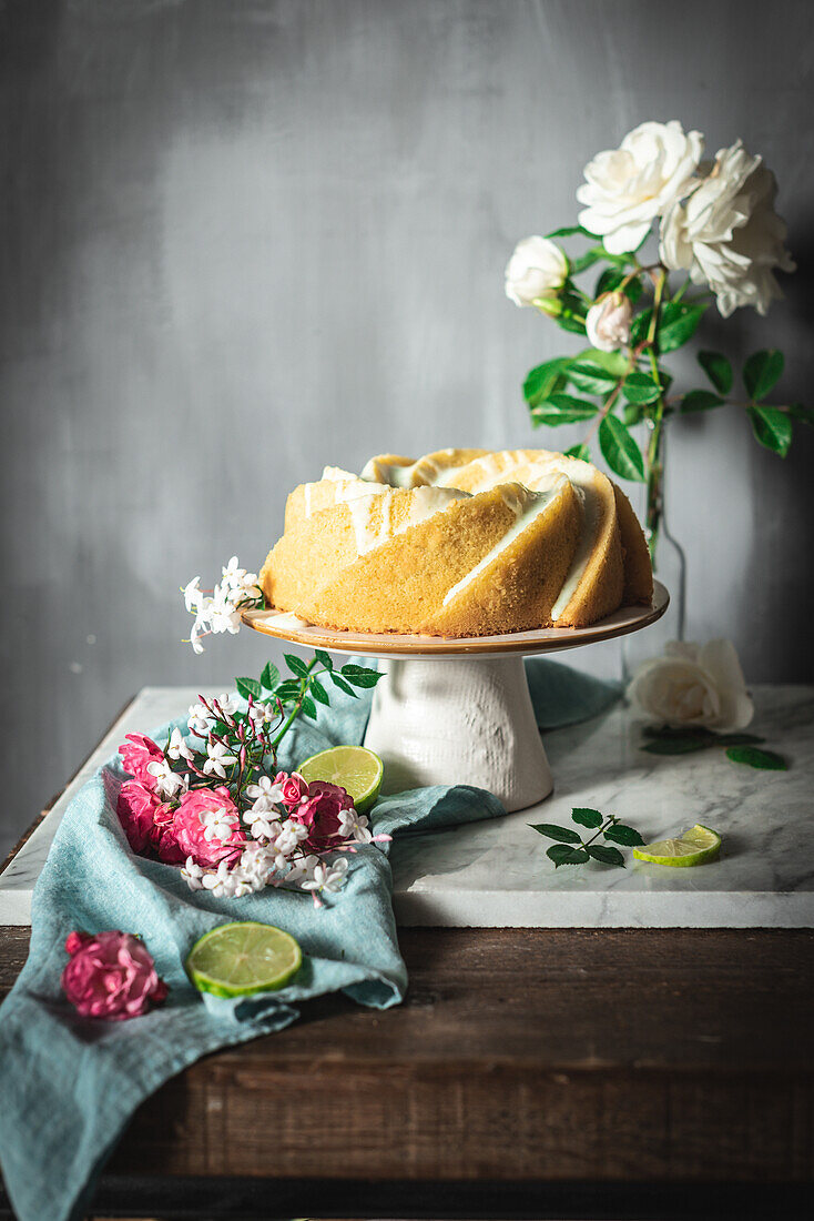 Tasty lime sponge cake served on white plate near flowers and lime slices