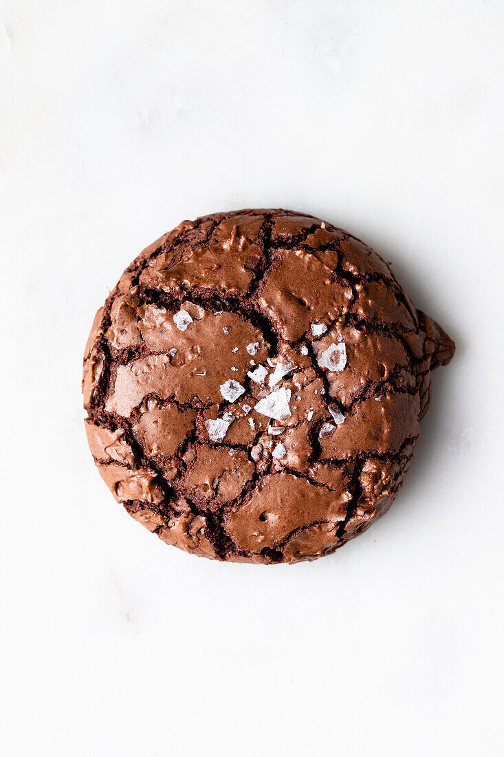Draufsicht auf einen süßen, frisch gebackenen Schokoladen-Brownie-Keks mit Rissen auf weißem Hintergrund in einer hellen Küche zu Hause