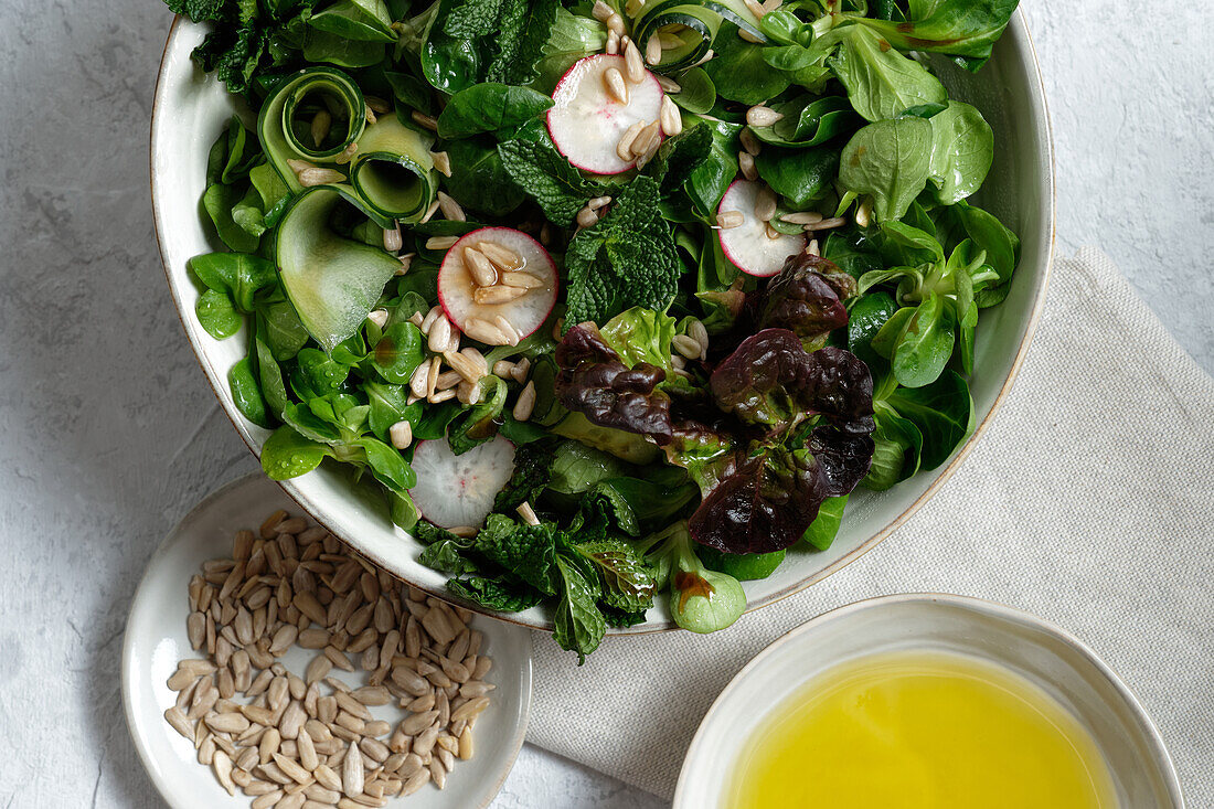 Top view of fresh healthy vegetable salad in bowl served on table with olive oil and sunflower seeds