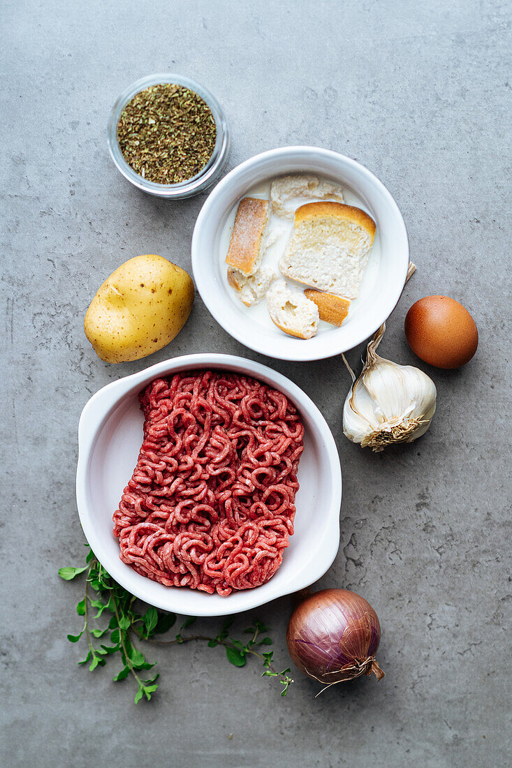 Top view of raw minced beef near bread and onion on gray background while preparing for traditional Greek keftede meal