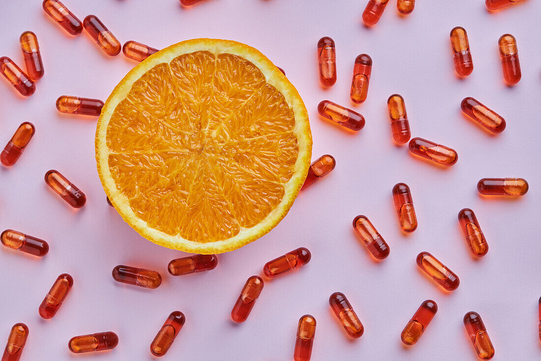 Top view composition of ripe cut oranges arranged on pink surface near scattered pills in light studio