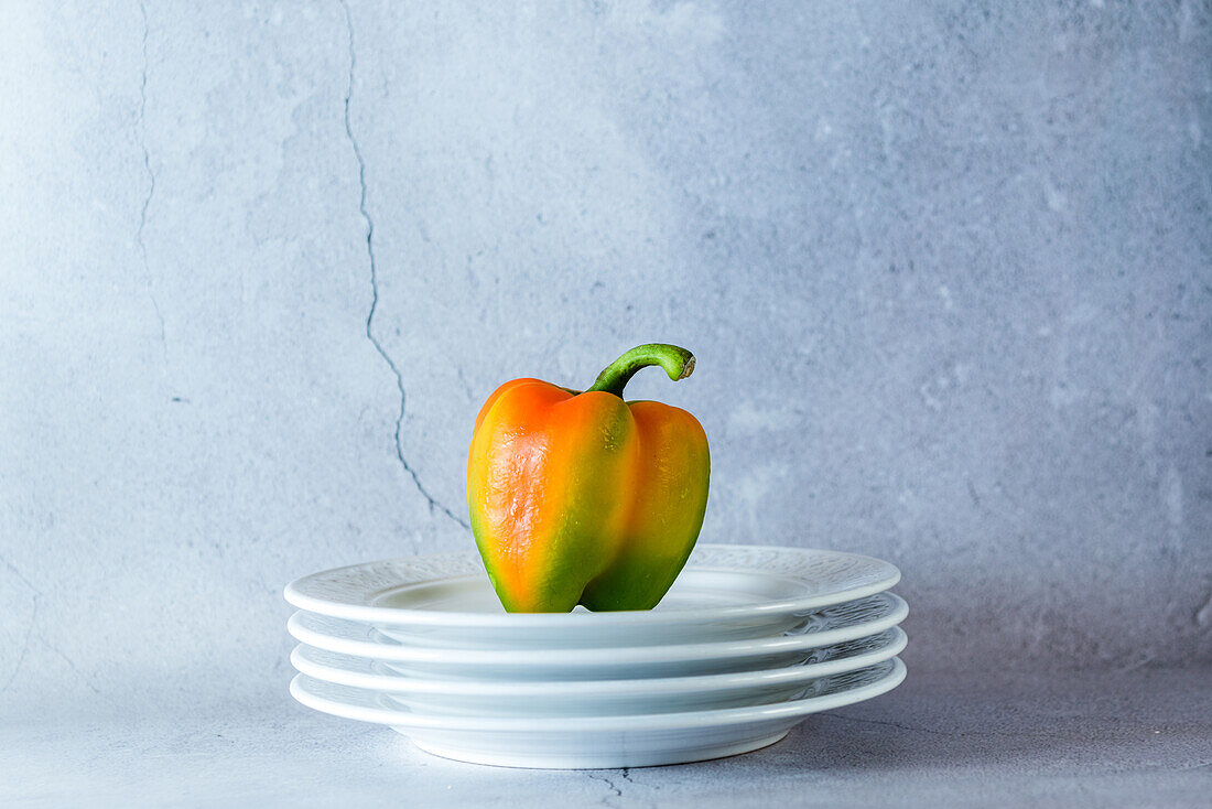 Still life composition with fresh colorful bell pepper placed on stacked white plates against shabby gray wall