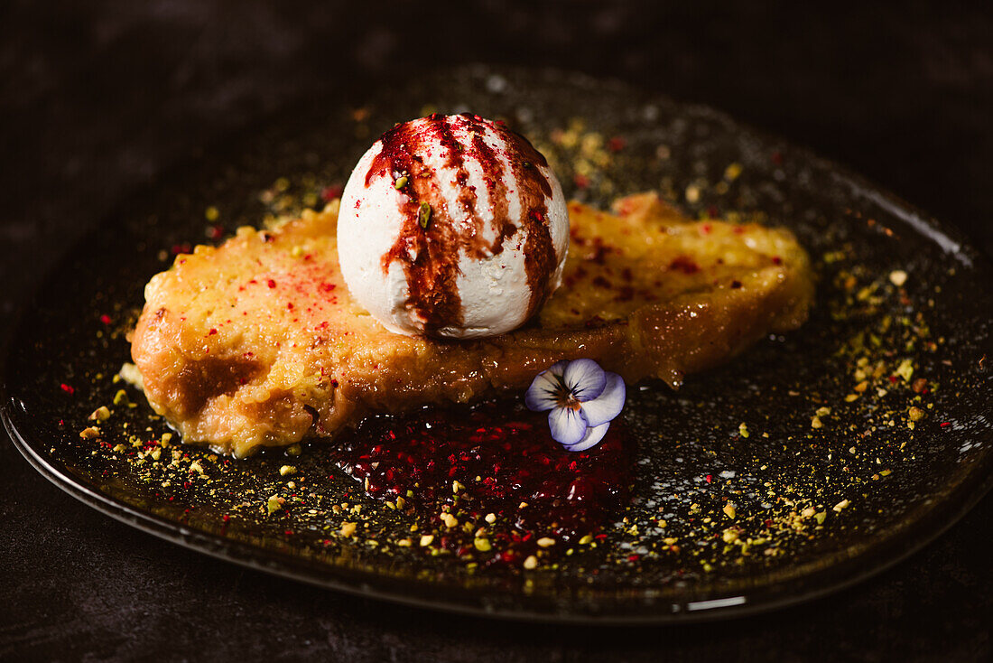 Yummy French toast with meringue milk ice cream scoop covered with sweet berry sauce on plate with condiments in restaurant on dark background
