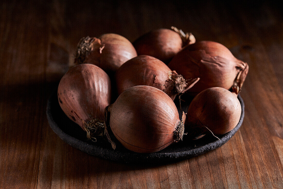 Bunch of fresh unpeeled onions placed on plate on timber table