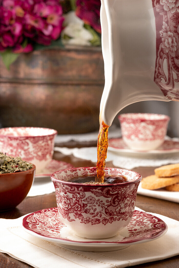 Aromatic hot tea being poured in ceramic cup placed on table for breakfast at home