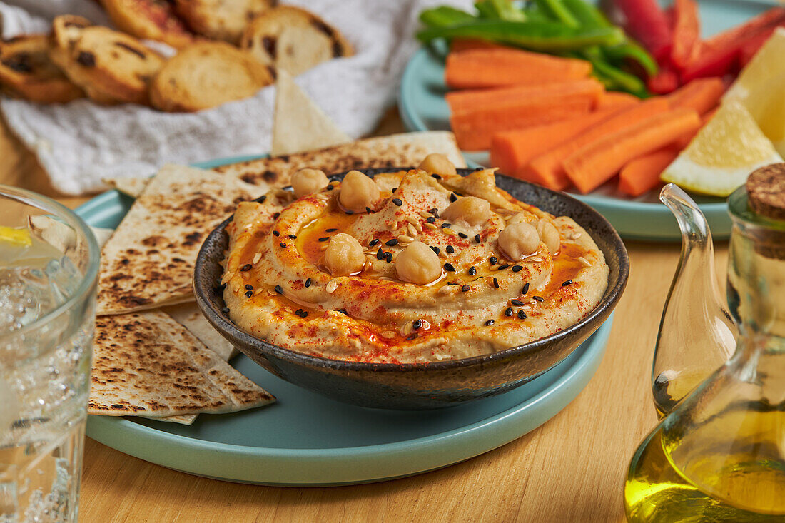 Leckerer Hummus und Tortilla-Chips auf einem Teller mit verschiedenen Gemüsesorten und Croutons und einem Glas kalter Limonade auf einem Holztisch (von oben)