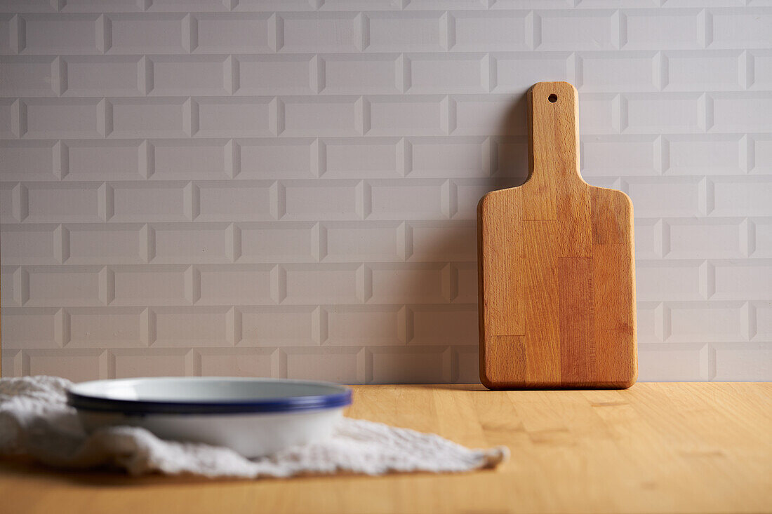 Wooden chopping board placed near wall on table with bowl in light kitchen