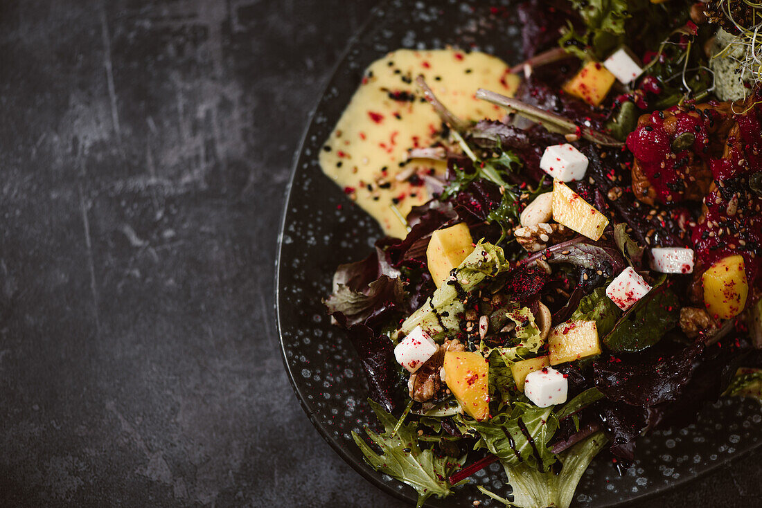 Draufsicht auf einen Teller mit leckerem vegetarischem indonesischem Salat mit frischer Mango und Cashew-Käse-Scheiben neben Sojabohnen und Gewürzen mit Basilikum-Vinaigrette