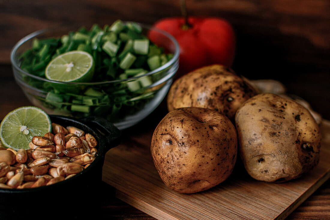 High angle of raw potatoes and chopped spring onion placed on wooden cutting board near bowl with grains prepared for cooking chicken broth