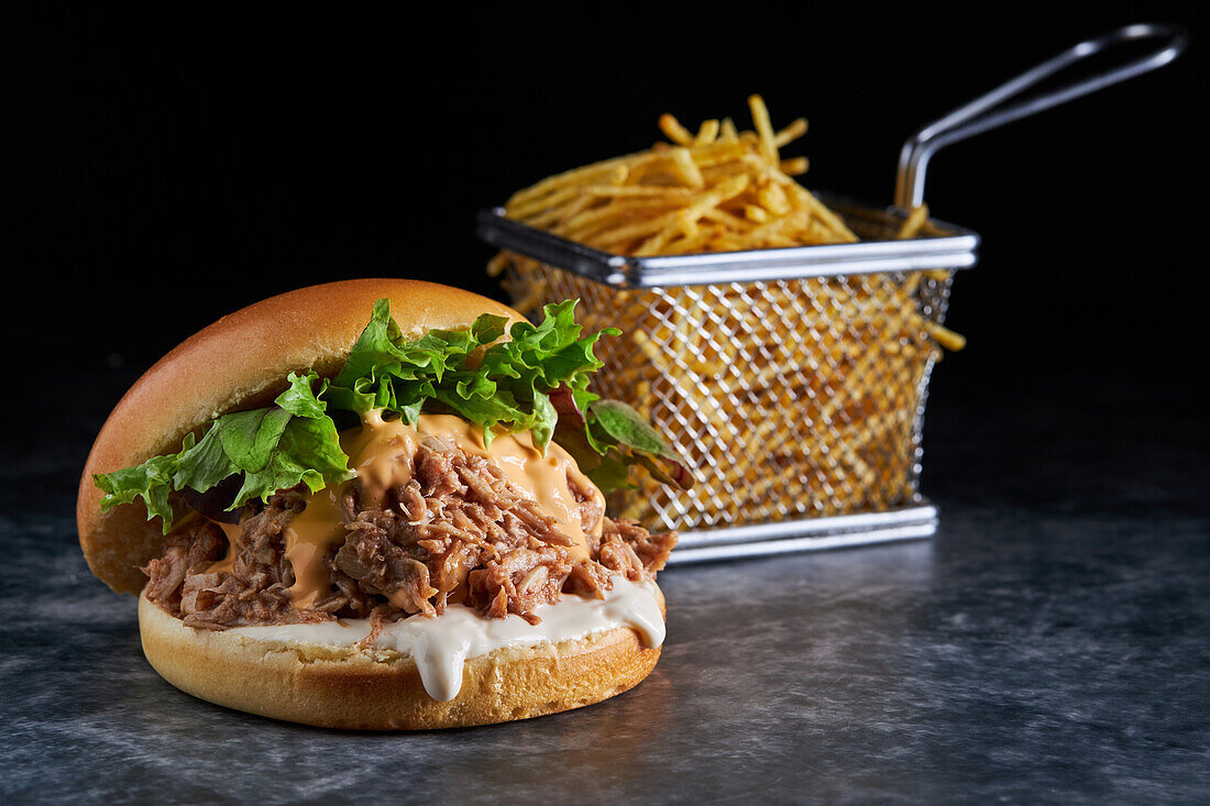 Yummy burger consisting of brioche bread smeared with mayonnaise and pork with barbecue sauce cheddar cheese and lettuce mix served with French fries