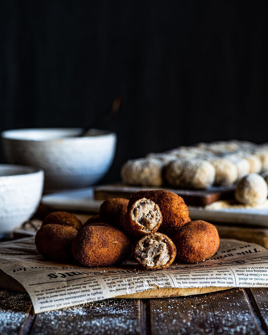 Delicious fried croquettes rolled in bread crumbs placed on piece of newspaper on wooden board