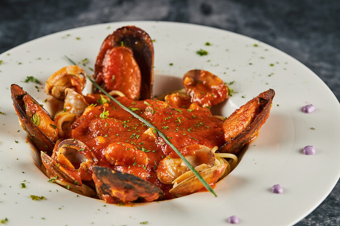 Nahaufnahme von Meeresfrüchtespaghetti mit Tomatensoße, die auf einem Teller auf schwarzem Hintergrund in einem Restaurant serviert werden