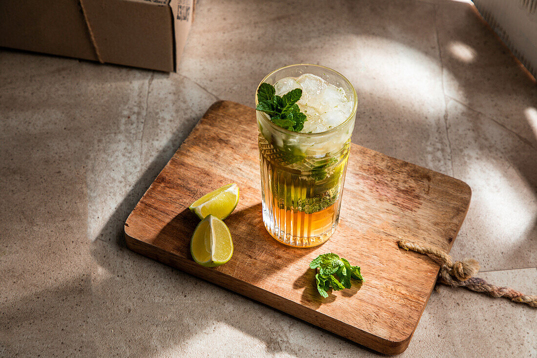 From above of refreshing cold alcoholic mojito with ice mint leaves and cut lime on wooden board