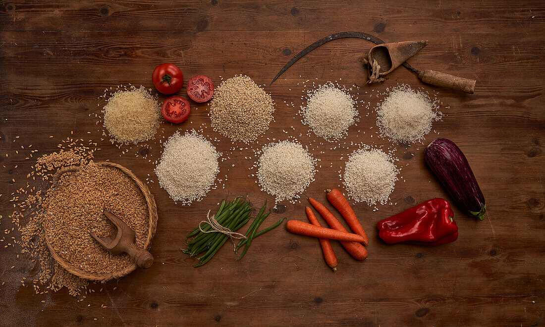 Top view of arranged small heaps of organic grains with fresh tomatoes and beans and other vegetables on wooden table near sickle and bunch of wheat