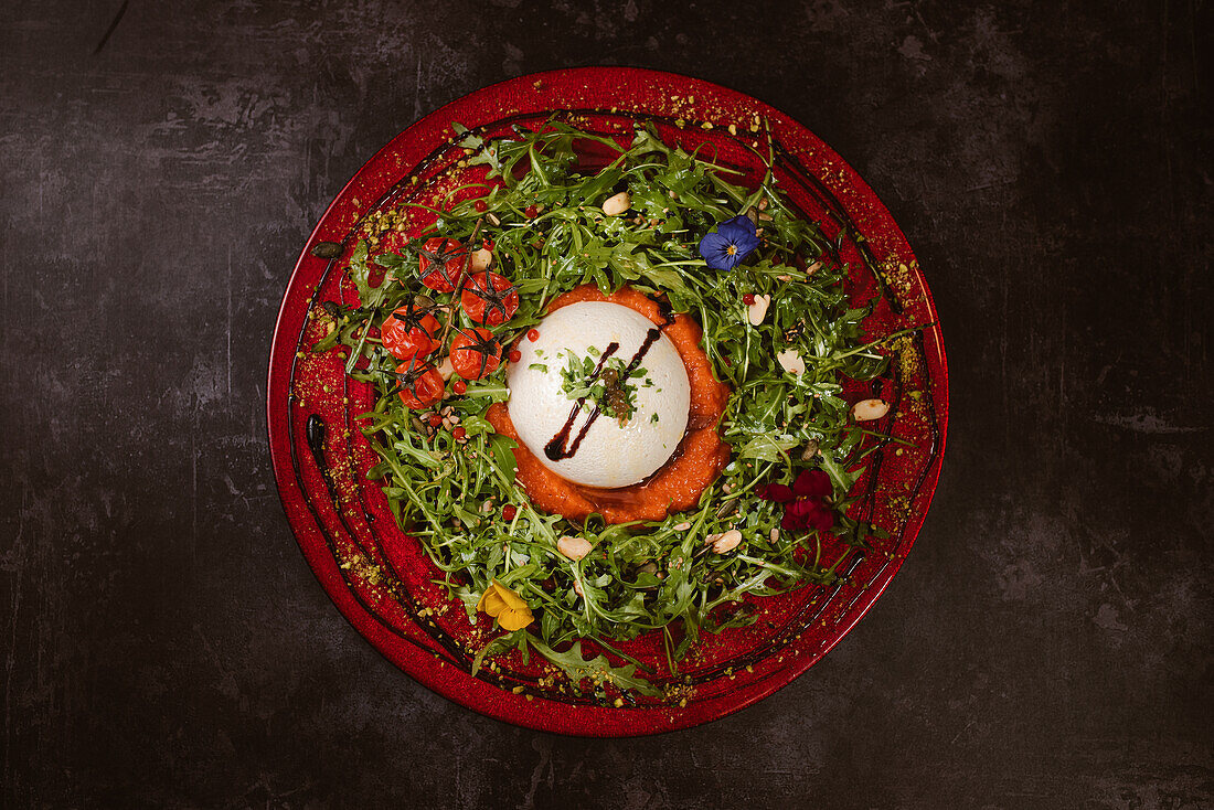 Overhead view of yummy burrata cheese on cold tomato cream with arugula leaves and cherry tomatoes with truffles and peanuts