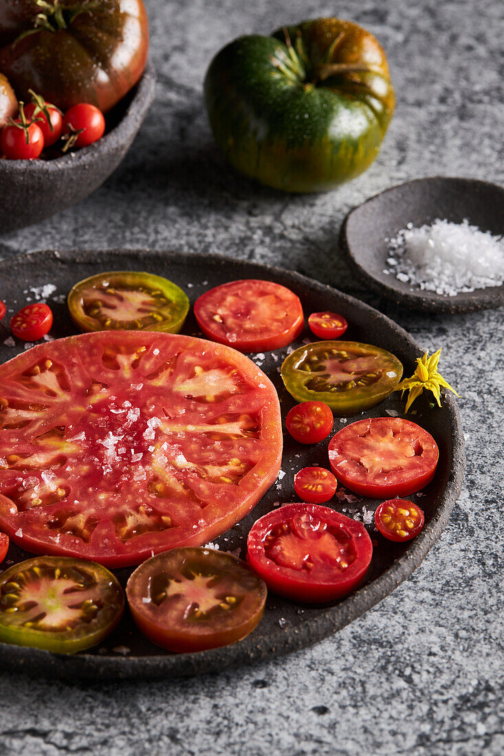 From above of delicious sliced tomatoes in cast iron plate near sea salt and jug of olive oil on concrete table