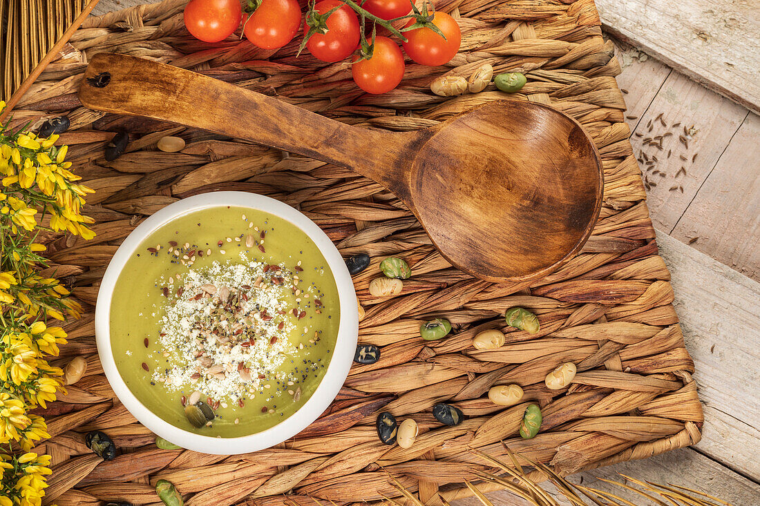 Draufsicht auf eine appetitliche vegane Cremesuppe mit zerstoßenen Pistazien auf einer Weidenmatte mit Holzlöffel