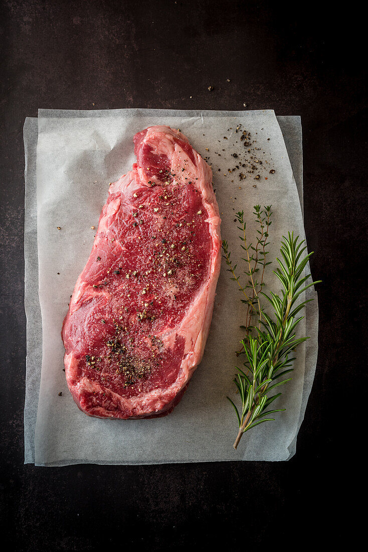 Overhead view of uncooked meat piece with thyme leaves against paper on black background