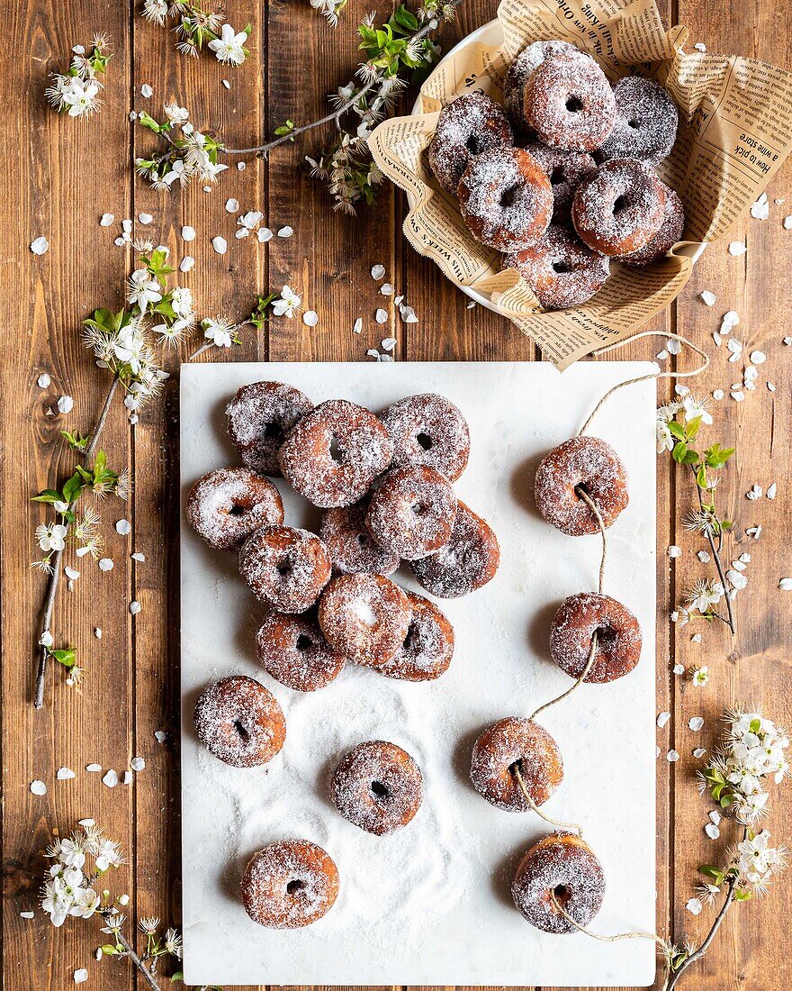 Draufsicht auf appetitanregende geliehene Donuts, die auf einer weißen Tafel auf einem Holztisch mit Blumen angeordnet sind