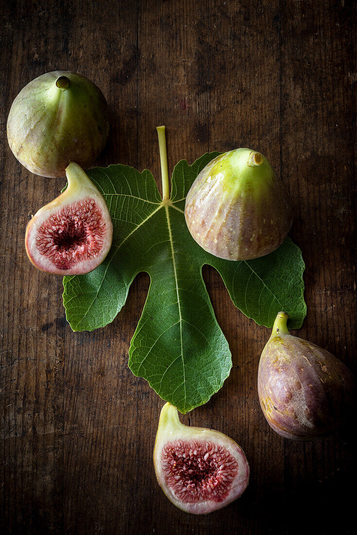 Top view of ripe halved and whole figs placed with green leaf on wooden rustic table