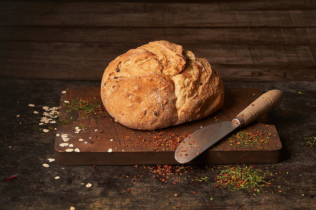 Appetizing aromatic freshly baked homemade bread with raisins placed on wooden board sprinkled with herbs