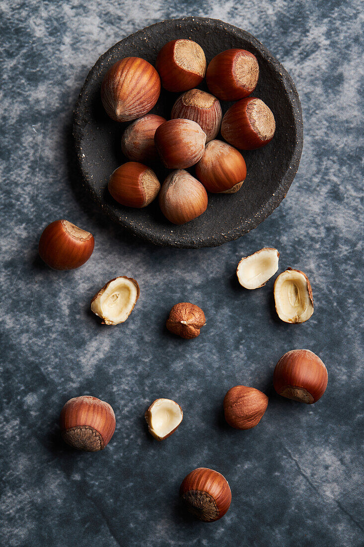 From above bunch of ripe hazelnuts in bowl and shells on marble table