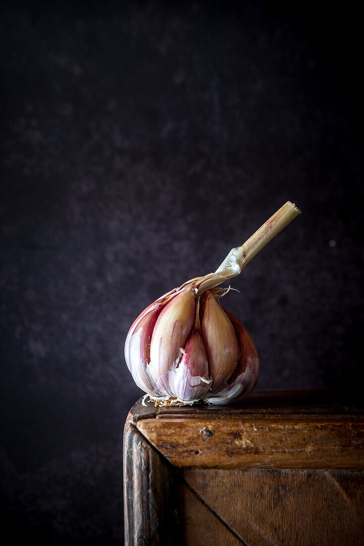 Whole head of fresh garlic placed on shabby wooden table in rustic kitchen with dark background