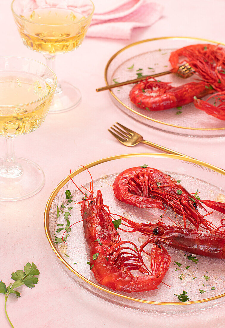 From above glass plate with tasty fried tiger shrimps placed near glass of wine on table pink background
