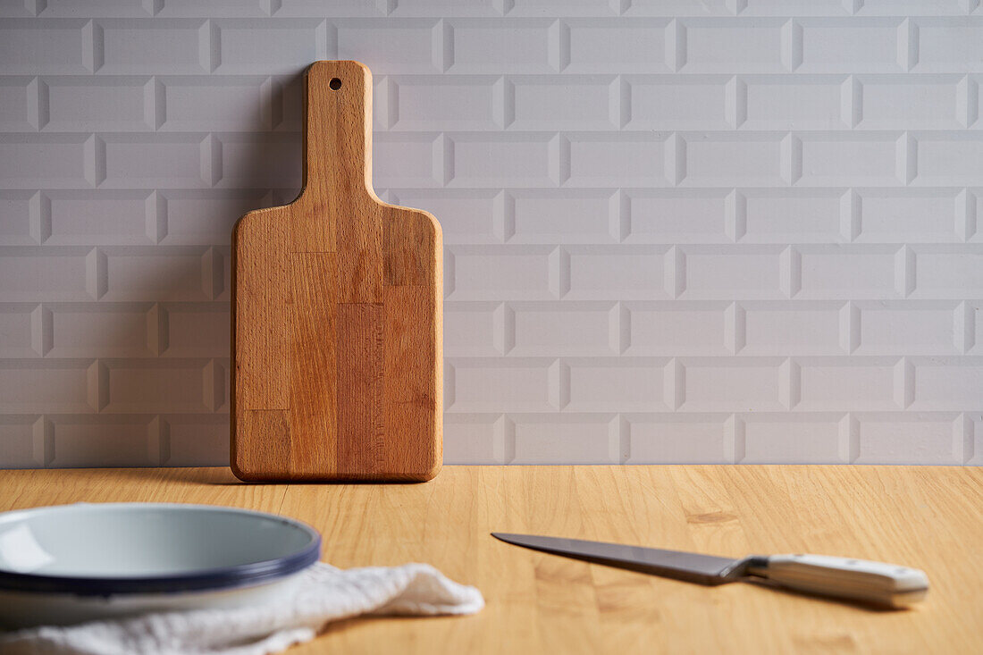 Holzschneidebrett in Wandnähe auf Tisch mit Schüssel und Messer in heller Küche