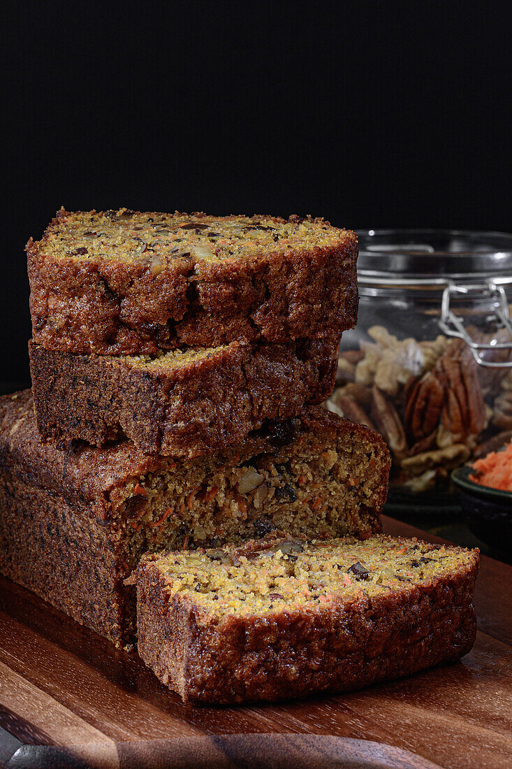 Carrot cake cut into pieces stacked on a wood next to a jar full of walnuts