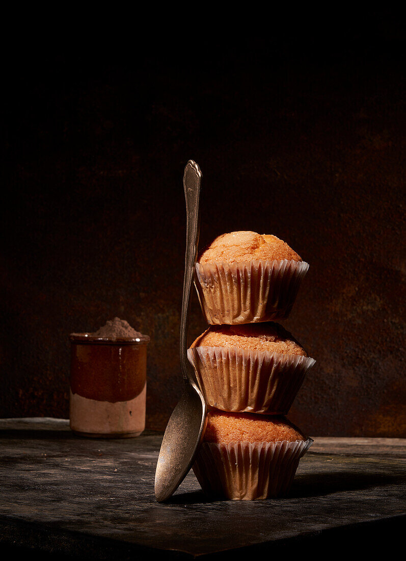 Tasty sweet baked muffins stacked on top of each other near spoon on black background