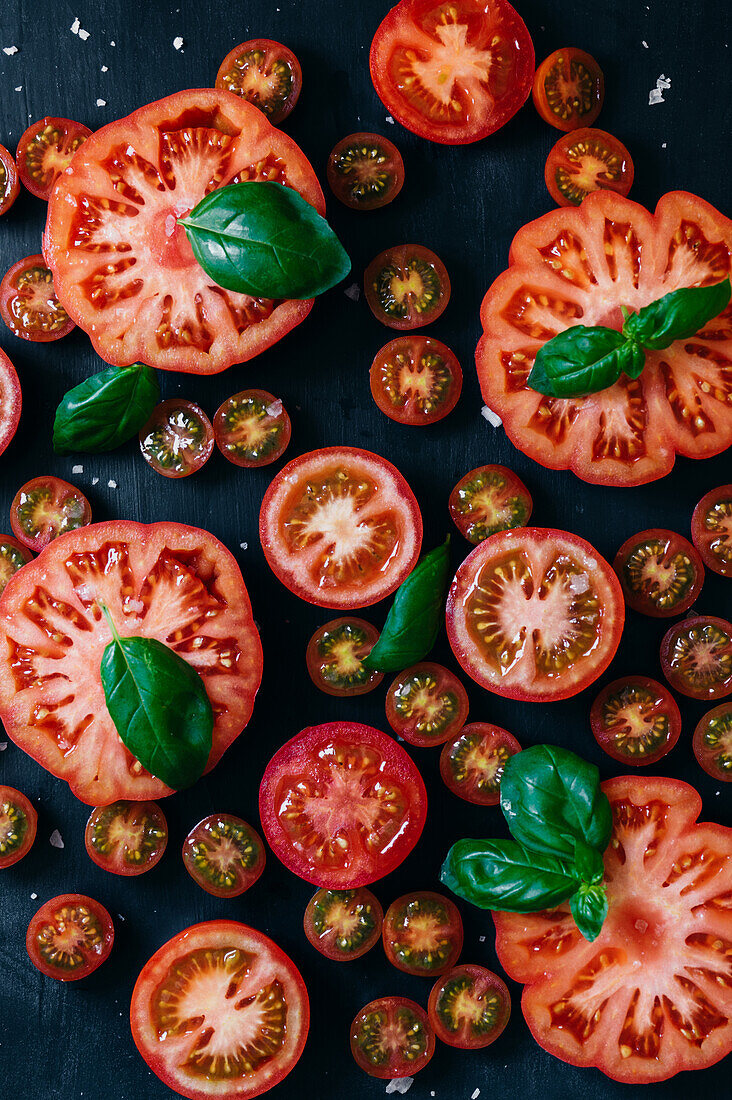 From above half cut tomatoes on table with basil leafs