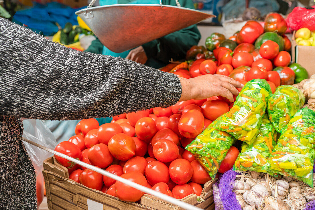 Anonymer Kunde streckt die Hand nach reifen roten Tomaten aus, während er Gemüse auf einem Wandermarkt in der Stadt Cusco auswählt