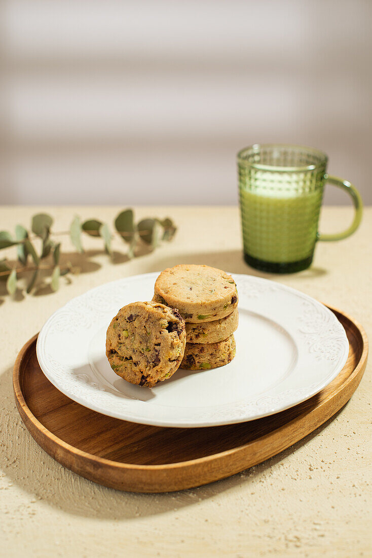 Plate with stack of tasty biscuits and mug of fresh milk placed on table near napkin and vase with twigs in morning