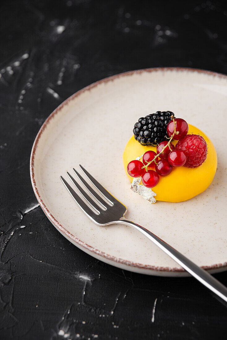 From above yummy small cake with various natural berries served on plate near fork on black table