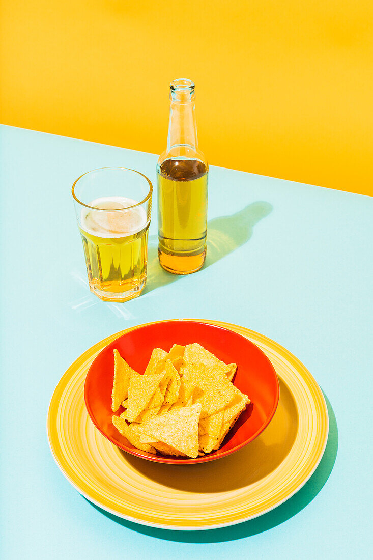 Schale mit knusprigen Tortilla-Chips neben Glas und Flasche mit kaltem Bier