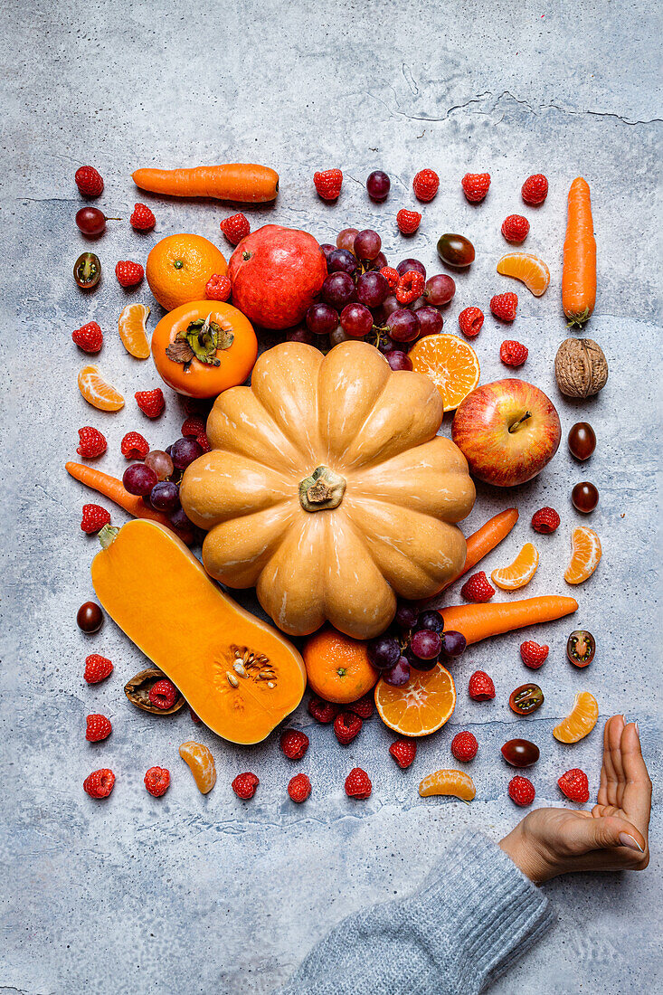 Hand showing still life of assorted autumn veggies, pumpkins, apples, persimmons, tangerines, grappes and hazelnuts from above