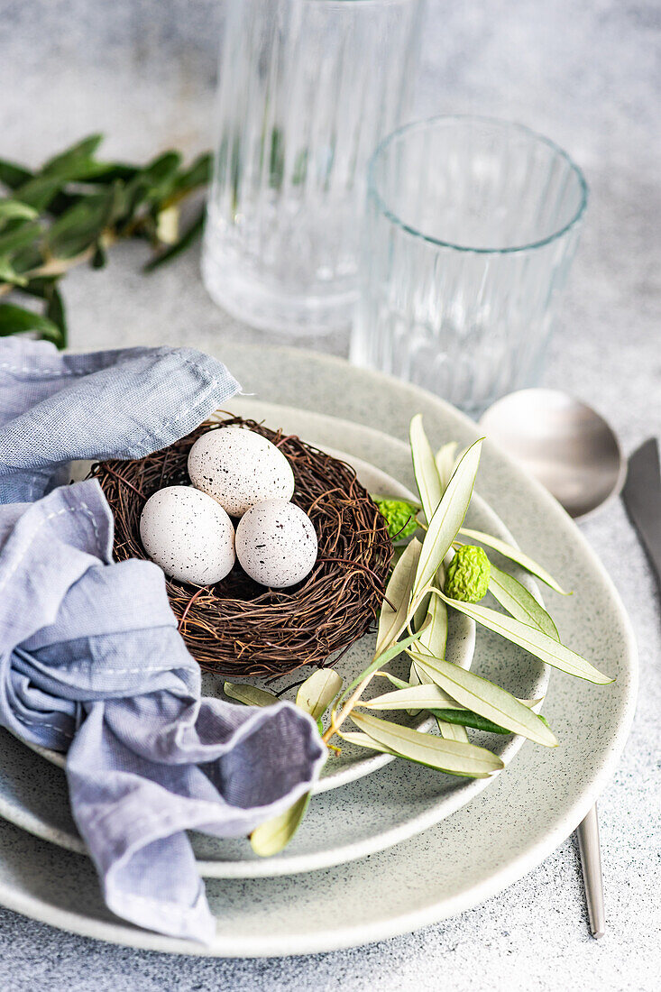 Besteckset für das Osteressen mit Olivenzweigen und Eiern auf einem Vogelnest auf einem Betonhintergrund